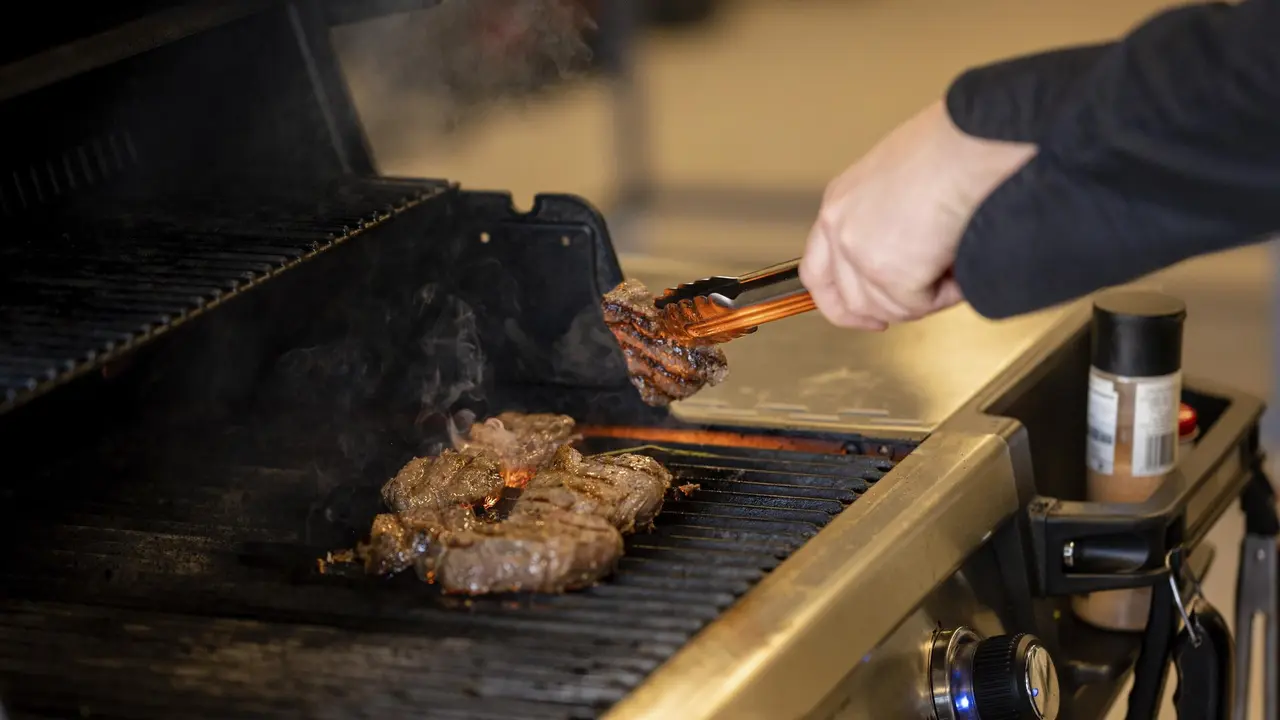 Un cocinero preparando carne a la parrilla. FREEPIK