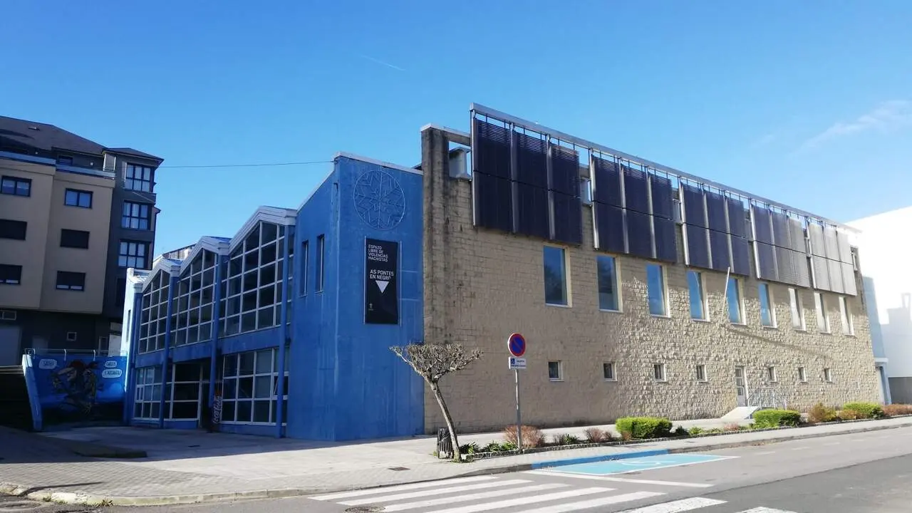 EXTERIOR DE LA PISCINA MUNICIPAL DE AS PONTES. CARTEL DE AS PONTES EN NEGRO, CONTRA LA VIOLENCIA MACHISTA. PASO DE CEBRA, SEÑAL DE ESTACIONAMIENTO PROHIBIDO